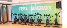 A row of exercise bikes under a turquoise wall that reads 'FEEL THE ENERGY'