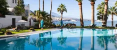 Guest in blue robe walking by a pool with palm trees and a sea view