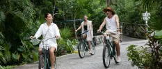Two women and a man riding bikes on a path surrounded by tropical greenery