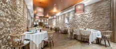 Restaurant with large-stone walls, tables with white tablecloths and wooden chairs laid out for meals