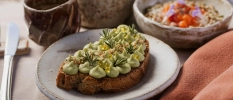 Piece of bread with an avocado spread and a bowl of muesli for breakfast
