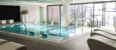 Sleek indoor pool surrounded by cubist crea, loungers and floor-to-ceiling windows