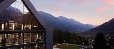 Exterior of Lefay Resort & Spa Dolomiti, angular building with full-length windows overlooking mountain peaks and a twinkling village below