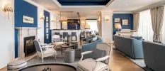 Cosy lounge with blue walls and sofas, a grey rug, gold lighting and white chairs with grey/blue cushions