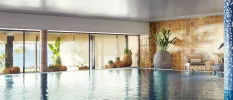 Large indoor pool surrounded by terracotta plant pots, floor-to-ceiling windows and blue tiled columns