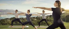 Group stand in warrior pose during a yoga session in a garden overlooking mountains