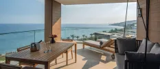 Large oceanfront balcony with a wooden dining table, cushioned hanging seat and loungers