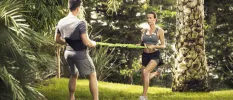 Man and woman in grey active wear work out using an elasticated rope in a lush garden setting
