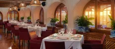 Colonial-style restaurant with cream walls and wooden ceiling beams, swooping archways, plants in blue and white china pots and crisp white tablecloths