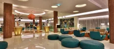 Modern reception with a glossy tiled floor, oversized gold plant pots and a hanging orange ceiling light, teal bean bags and sofas