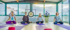 Group of woman on their knees on yoga mats with eyes closed and a sound gong behind them