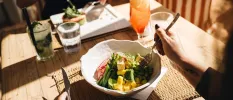 Two people sat down to eat at a table, one with vegetables in a bowl and an orange coloured drink beside her