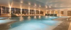 Indoor swimming pool at night-time, as seen through surrounding windows, with LED lighting and water jets