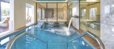 Spa area with a rectangular pool with jets, terrace with white loungers, floor-to-ceiling windows and spotlights