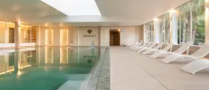 Indoor pool with LED lighting, a neighbouring terrace with white loungers and large windows