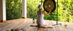 Woman in a white dress and headscarf playing a gong, sitting in an open-air pavilion