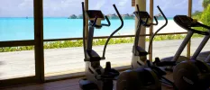 Bike machines in a gym with floor-to-ceiling windows overlooking white sands and turquoise shallows