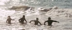 Two men and two women in wetsuits clamber out of the sea in the sunshine