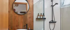 Wooden bathroom with white sink, black hanging mirror and shower with black bottles