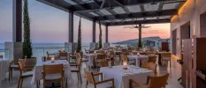 Outdoor restaurant terrace at sunset with tables laid out with crisp white tablecloths and an ocean view