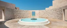 Sunny stone-walled courtyard with a pond with turquoise water at the centre