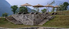 Cobbled stone walls and grassy hills next to a terrace of loungers and parasols and a mountain view