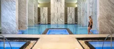 Indoor swimming pool and plunge pools surrounded by marble pillars, and a woman in a black swimsuit making her way into the water