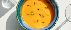 Blue bowl with an orange-coloured soup with a herb garnish