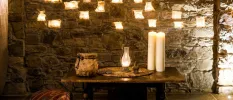 A stone wall and wooden table with candles places in the brickwork and on the table