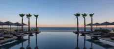 Infinity pool at sunset, with the outline of sun loungers and parasols and tall palm trees at the edge
