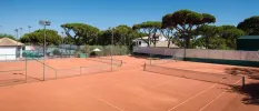Terracotta-hued tennis courts surrounded by gardens under a blue sky