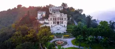 Colonial Indian palace on a hillside among trees and shrubs, with a landscaped roundabout in front