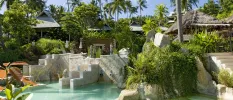 Tropical gardens, stone pathways, steps and parasols framing a grotto-like pool