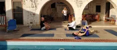 Three people stretching on blue yoga mats next to a pool, as an instructor watches on and the sun comes up