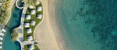 Aerial view of a swimming pool, lawn with loungers and parasols, sandy beach and the sea