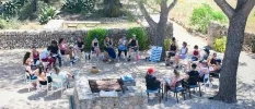 Group sit in chairs in a circle in a stone courtyard surrounded by greenery