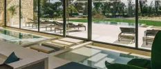 Indoor pool with stepped walkways and entry points, in front of floor-to-ceiling windows overlooking an outdoor pool