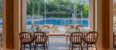 Restaurant with wooden tables and chairs, full-length glass doors and a view of the pool