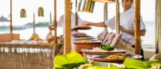 Pots of food lined up buffet-style with a chef in whites behind, and the ocean in the background