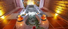 Bath filled with water and leaves in a candelit room with tiled floors and stone walls