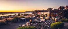 Outdoor courtyard with shrubs and seating overlooking the ocean at sunset