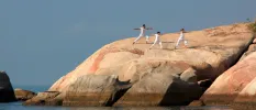 Three people in white in a yoga pose on a rock face on a sunny rock formation