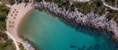 Aerial view of a sandy bay lapped by clear turquoise shallows and surrounded by rocky cliffs