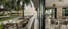 Modern restaurant with indoor and outdoor tables, full-length glass and a view of the ocean and palm trees