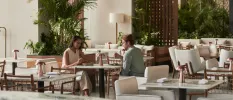 A man and woman sitting down eating in a neutral. airy restaurant with lots of tropical greenery