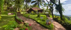 Traditional Indian buildings spread among lawns, pathways and coconut palms with the ocean in the background