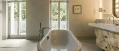 Marble bathroom with freestanding bath, mirror with light bulbs surrounding it and floor-to-ceiling windows