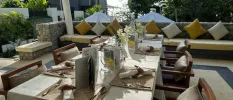 Stylish al fresco restaurant terrace with cobbled walls, yellow cushions and seat pillows, surrounding gardens and white umbrellas