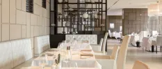 Airy restaurant with glossy tiled walls, dark-wood shelves stacked with ornaments, and white tablecloths