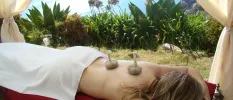 Woman lies on her front with herb parcels on her back in an open-air treatment cabin